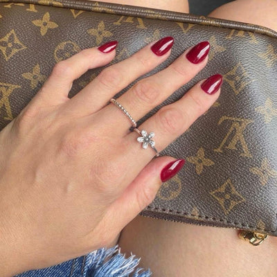 A hand wearing short almond deep red press on nails rests on a brown Louis Vuitton monogram handbag, accented by a delicate floral silver ring on the ring finger.