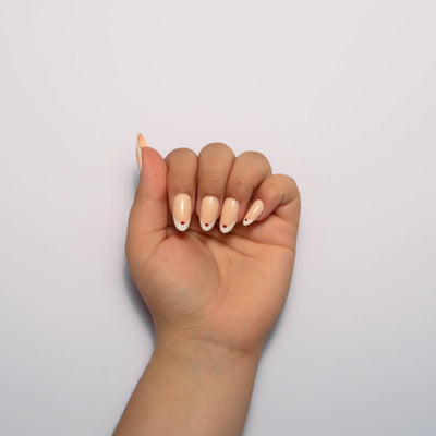 A hand curled into a loose fist against a plain white background, displaying medium oval nude press on nails with a white french tip and a tiny red heart accent at the cuticle.