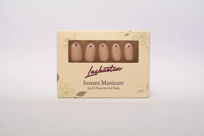 A box of Lashnetix 'Instant Manicure' press-on nails against a white background. The packaging is cream-colored with gold floral sketches and displays medium oval nude with white french tip and red heart accent nails through a clear window.