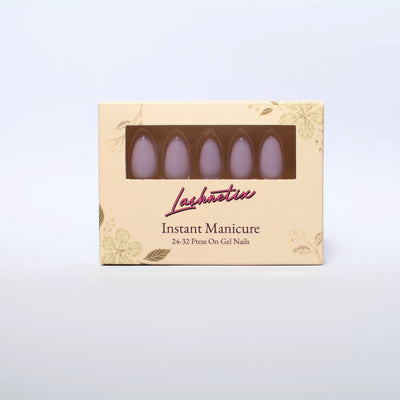 A box of Lashnetix 'Instant Manicure' press-on nails against a white background. The packaging is cream-colored with gold floral sketches and displays short almond lavender through a clear window.