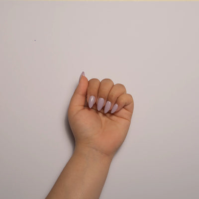 A hand curled into a loose fist against a plain white background, displaying short almond lavender press on nails.