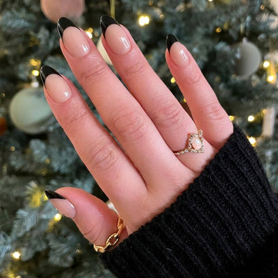 Hand with black nail polish and rings in front of a decorated Christmas tree