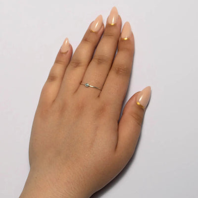Hand with beige nail polish and a gold ring on a light gray background