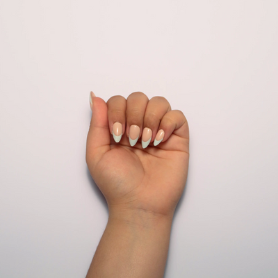 A hand curled into a loose fist against a plain white background, displaying short almond nude press on nails with a sage green french tip.