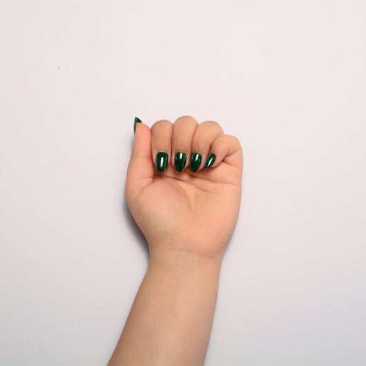 A hand curled into a loose fist against a plain white background, displaying short oval green press on nails.
