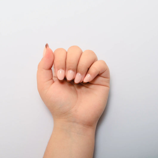 A hand curled into a loose fist against a plain white background, displaying short oval nude french tip press on nails.